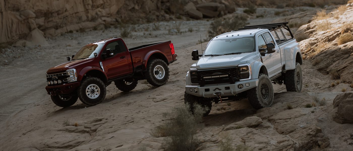 A red and a white Truman Motors Super Duty build on sandstone in a desert canyon