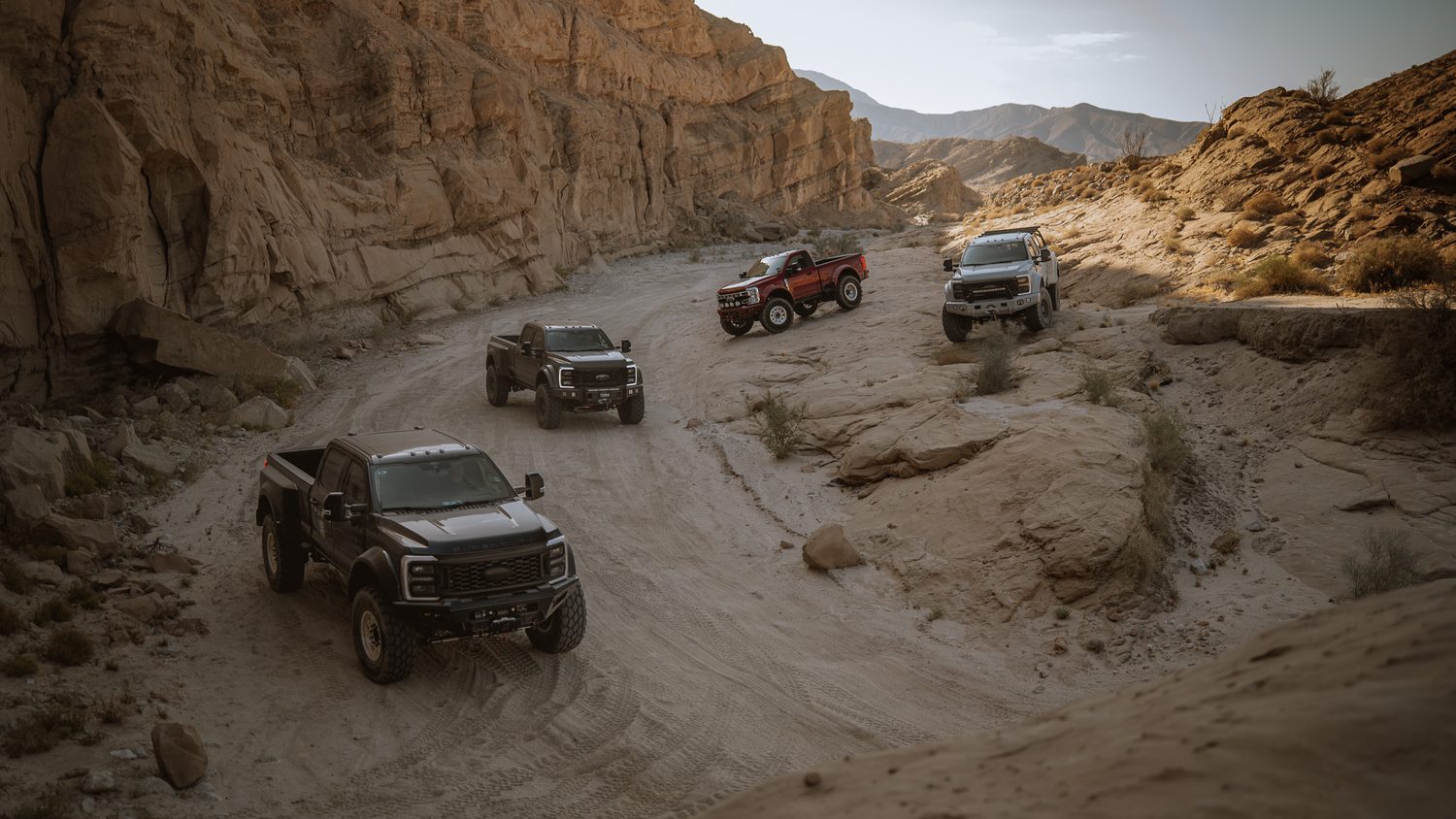 Four Truman Motors Ford Super Duty builds descending a desert canyon trail